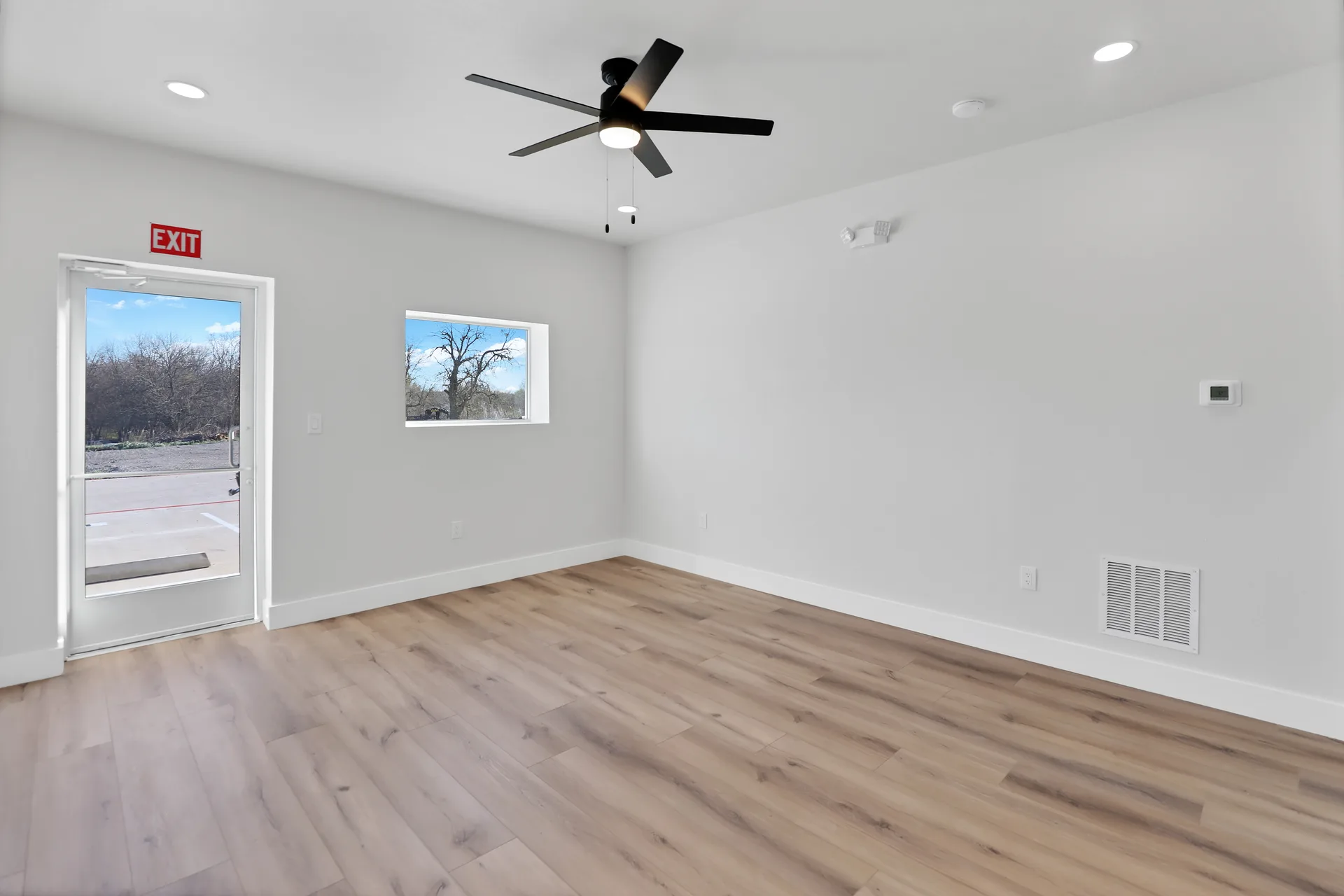 Office suite interior with exterior access door, window, HVAC vent, thermostat, and ceiling fan